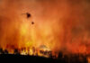 Helicopter fighting forest fire with water bucket.