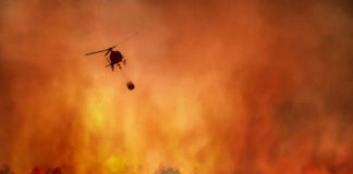 Helicopter fighting forest fire with water bucket.
