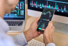 China CUTS Off Foreign Investments – What’s Next? Person checking stock market graphs on phone and monitors.