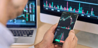 Person checking stock market graphs on phone and monitors.