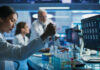Scientist using pipette at lab bench with test tubes and monitors