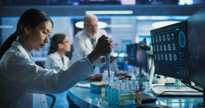 Scientist using pipette at lab bench with test tubes and monitors
