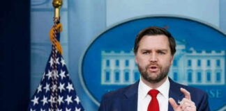 Man speaking at podium with American flag behind