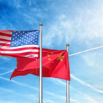 Flags of the United States and China waving against a blue sky