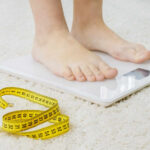 Person standing on a digital scale with a measuring tape nearby