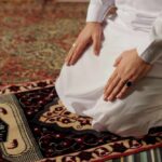 Person kneeling on a prayer rug in traditional attire
