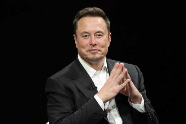 Man in black suit sitting, clasping hands.