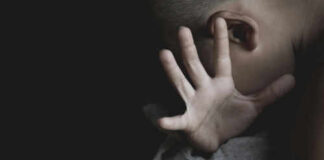 Child covering face with hand in dim light