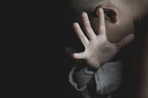 Child covering face with hand in dim light