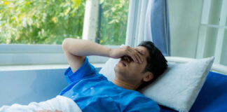 Man in hospital bed covering eyes with hand
