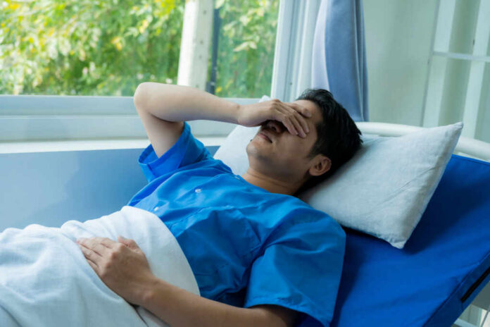 Man in hospital bed covering eyes with hand