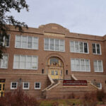 Historic brick school building with arched entrance and large white-framed windows