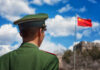 Is Your Money Funding China’s Military? Soldier in a green military uniform facing the Great Wall of China with the Chinese flag in the background