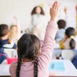 Students in a classroom raising their hands to answer a question