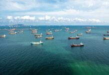 President Trump Says It’s Done—But Is It? Aerial view of numerous cargo ships anchored in a blue ocean