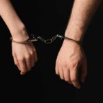 Two hands connected by handcuffs against a dark background