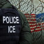 Suspect Rams Agent, Sparks Manhunt Police officer in tactical gear standing near a barbed wire fence with an American flag in the background