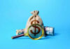 Trump Accounts Offer Kids $1,000 Head Start Money bag and magnifying glass on blue background