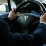 Technology Failed—or Did Someone Else? Tesla steering wheel held by driver in a car interior