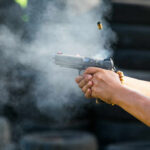 Hands firing a semi-automatic pistol with smoke and ejected casing