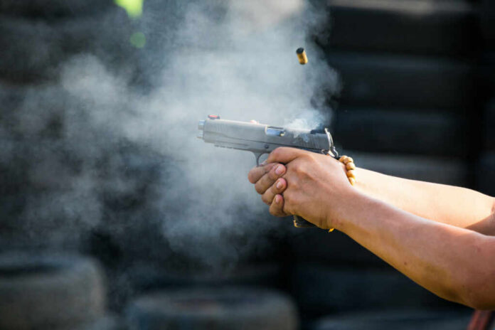 Hands firing a semi-automatic pistol with smoke and ejected casing
