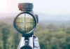 Rifle scope aiming at a forest canopy
