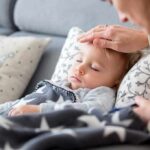 Sleeping toddler on couch with adult hand checking forehead