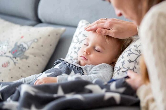 Sleeping toddler on couch with adult hand checking forehead