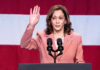 Woman raising her hand while speaking at podium.