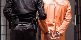 Prisoner in orange jumpsuit handcuffed with guard standing beside