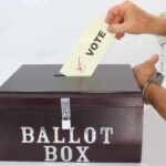 Hand in handcuffs casting a vote into a ballot box