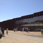 Border fence with group of people and a patrol vehicle