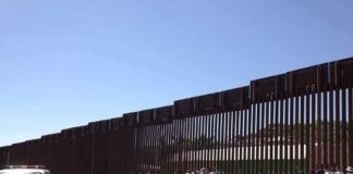 Border fence with group of people and a patrol vehicle