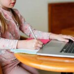 Child studying with laptop and notebook at a round table