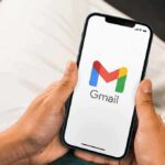 Hands holding a smartphone displaying the Gmail app logo