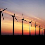 Wind turbines silhouetted at sunset over a flat landscape