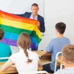 Teacher holding a rainbow pride flag in front of students