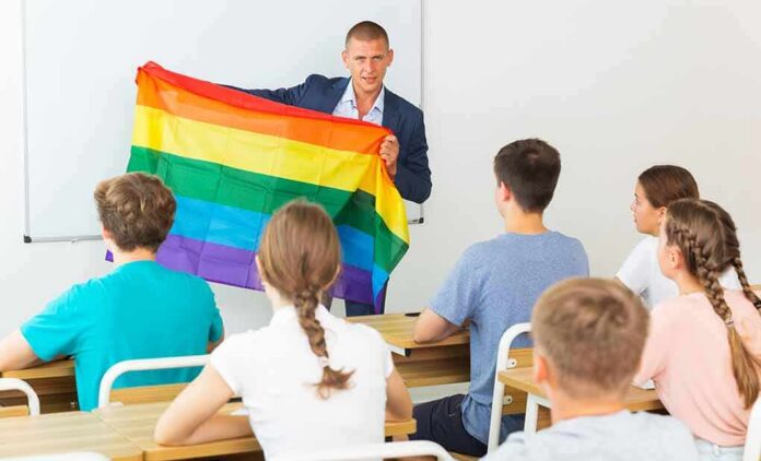 shutterstock_2023001951 Teacher holding a rainbow pride flag in front of students