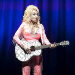 Singer in pink outfit playing a glittery acoustic guitar on stage