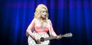 Singer in pink outfit playing a glittery acoustic guitar on stage