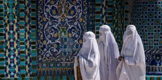 Three women in white veils walking past ornate blue tilework