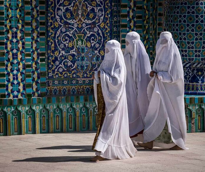 Three women in white veils walking past ornate blue tilework